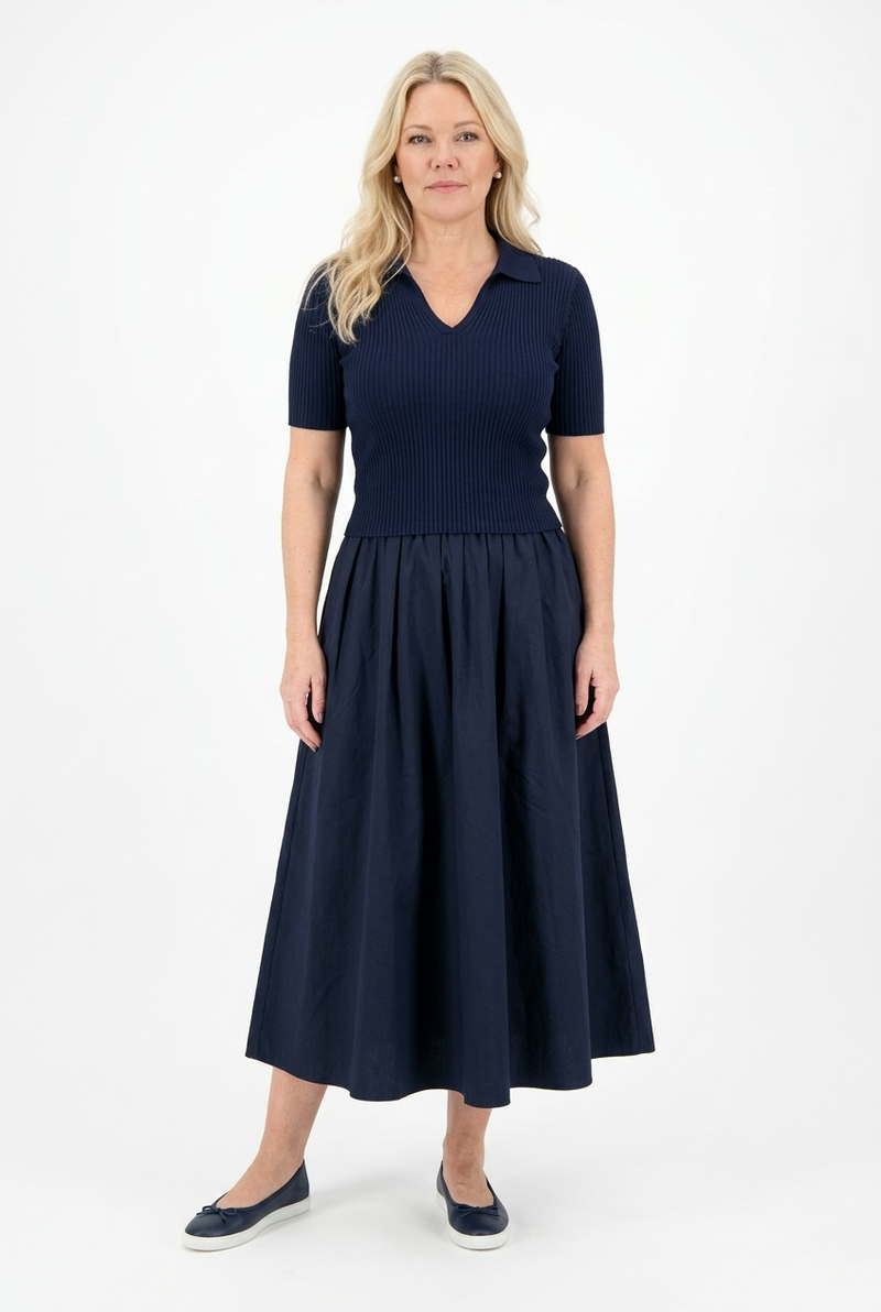 naisen päällä edestä kuvattuna midipituinen, tummansininen kellohelmainen ja lyhythihainen mekko, jossa istuva yläosa, v-pääntie sekä kaulukset ja alaosa kellohelmainen.