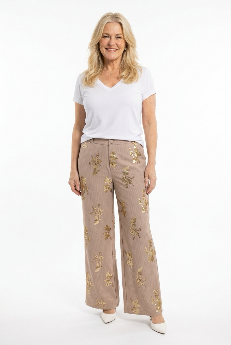 leveät täyspitkät beiget housut, joissa kullanvärisiä paljetteja ja vaaleita raitoja naisen päällä.