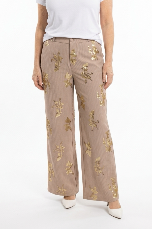 leveät täyspitkät beiget housut, joissa kullanvärisiä paljetteja ja vaaleita raitoja naisen päällä.