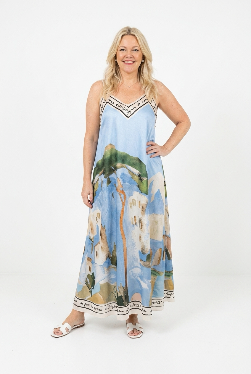 vaaleansininen a-linjainen maximekko naruolkaimilla. Mekossa suuri maisemakuosi ja tekstillä kantatut reunat ylhäällä ja helmassa. Mekko naisen päällä.