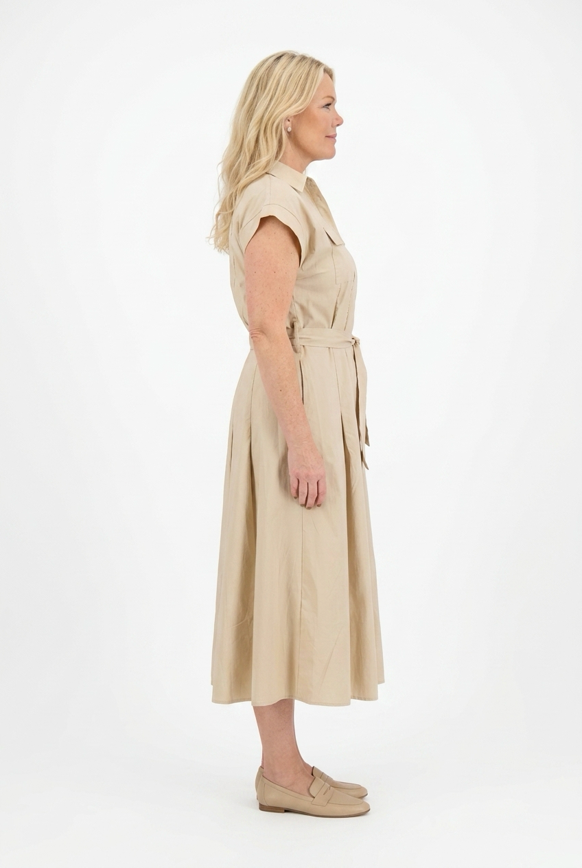 beige pitkä safarimekko lyhyellä hihalla naisen päällä. Mekossa kaulukset, napitus, kangasvyö ja taskut.