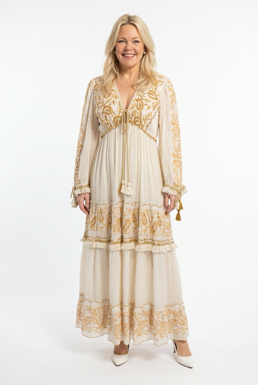 maxipituinen vaalea mekko pitkillä hihoilla. Mekossa ruskeita koristeita ja nyörejä. Mekko on kapea vyötäröltä ja helma levenevä.