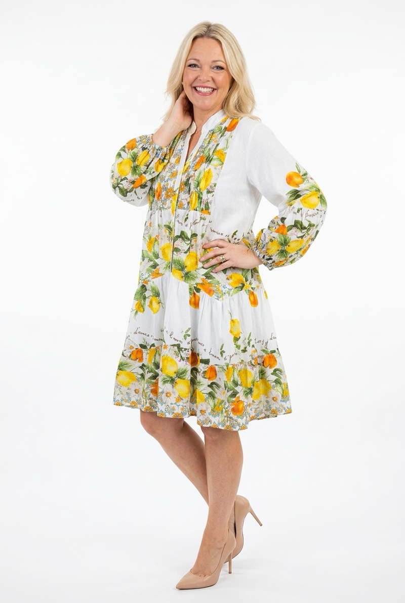 Valkoinen kellohelmainen polvipituinen mekko, jossa pitkät hihat ja sitruunakuosia naisen päällä.