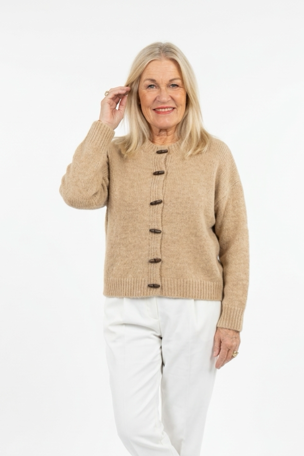 lyhyt ja pikähihainen beige neuletakki ruskeilla napeilla naisen päällä