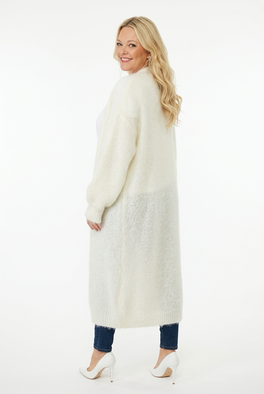 naisen päällä takaa kuvattuna ecrun värinen, polven alle pituinen neuletakki, jossa taskut edessä ja ei kiinnitystä.