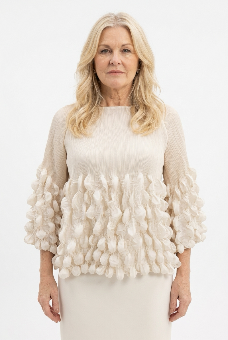 beige pusero naisen päällä, jossa 3/4 reilut hihat, lantiopituus ja venepääntie. Yläosa krepattua ja alaosa hihoista ja puserosta ilmavan kuplamaisesti koristeltu.
