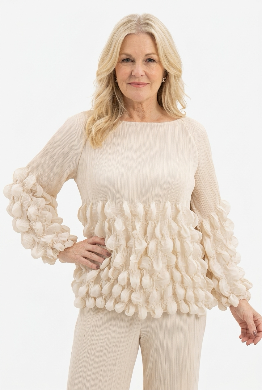 beige pusero naisen päällä, jossa 3/4 reilut hihat, lantiopituus ja venepääntie. Yläosa krepattua ja alaosa hihoista ja puserosta ilmavan kuplamaisesti koristeltu.