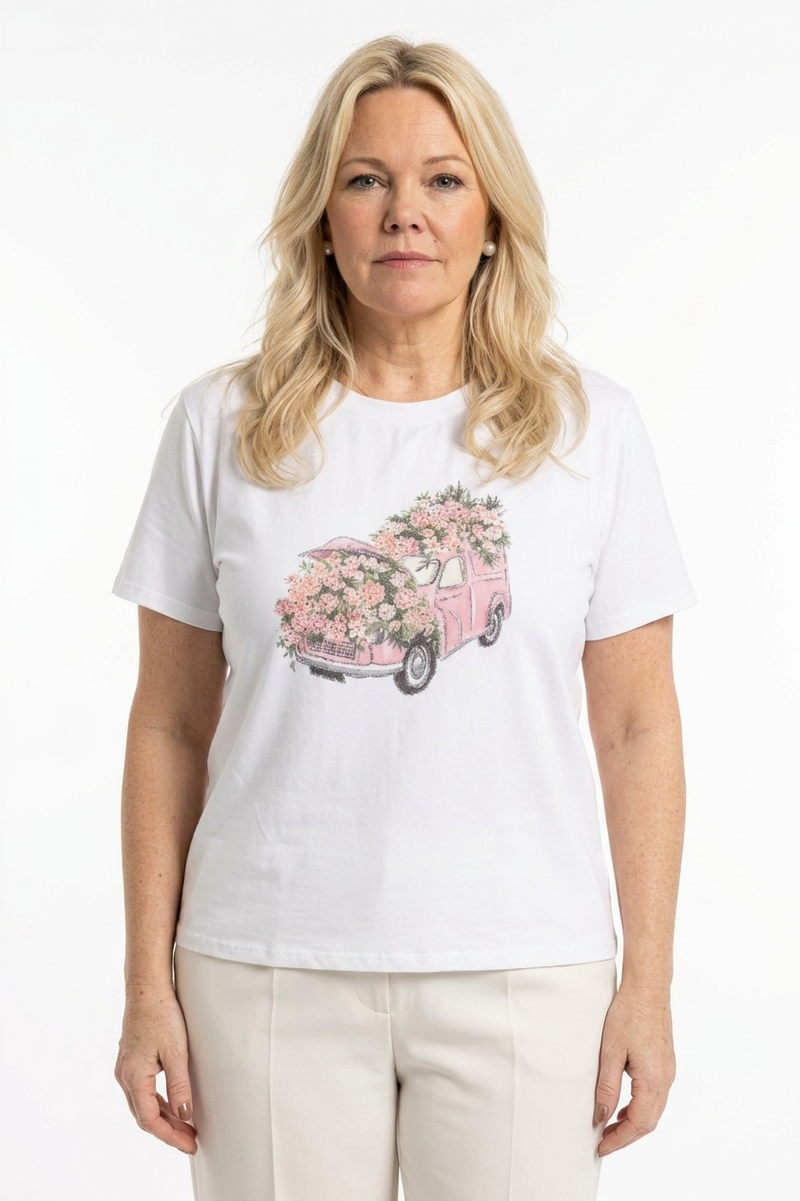 naisen päällä valkoinen t-paita lyhyellä hihalla ja o-pääntiellä, jossa kuvana  roosa auto sekä kukkia koristeltuna strasseilla edessä.